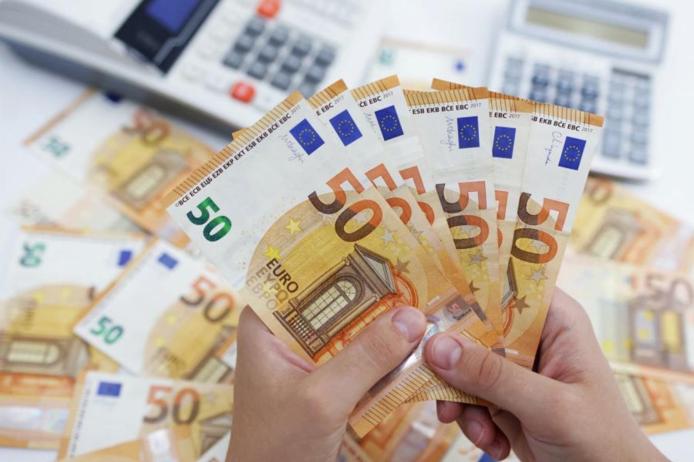 Des mains tenant des billets de 50 euros devant deux calculatrices, photo d'archives d'illustration