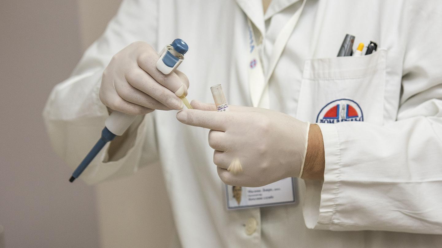 Mains gantées tenant une pipette et un tube d'échantillon devant une blouse blanche, image d'illustration