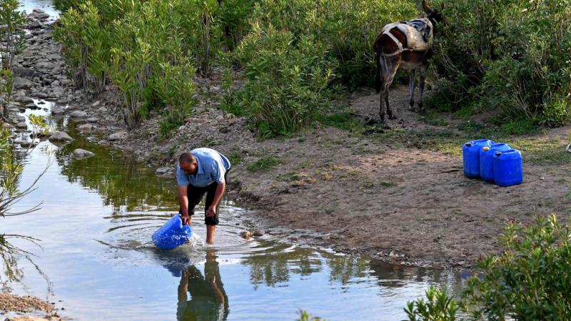Un homme remplit des bidons bleus dans un cours d'eau en Tunisie